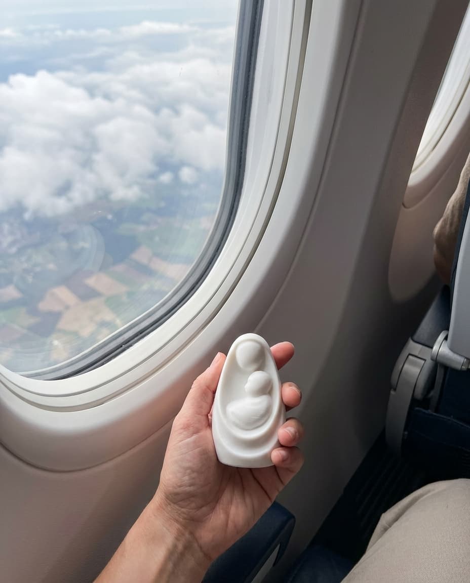 María en un Puño sostenida en la mano junto a la ventanilla de un avión, sobre las nubes
